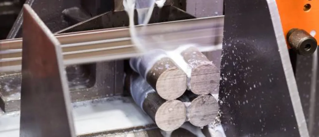 An orange saw cuts four steel rods as creamy-looking liquid streams down over the rods and flows down a silver chute.