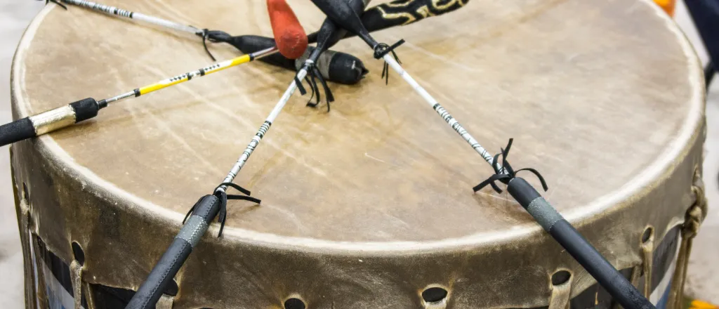 Indigenous wood and animal skin drum with six drumsticks resting on top
