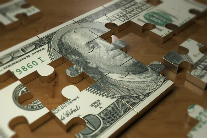 Metal puzzle of a United States one hundred dollar bill with pieces removed or missing.
