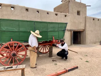 PICT Bent's Old Fort park staff greasing the axle of the park's green Conestoga Wagon. Courtesy NPS - Jake Koch