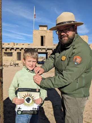 A Park Ranger pins a badge on a young Junior Ranger, who is holding a copy of the park's new Junior Ranger Book.