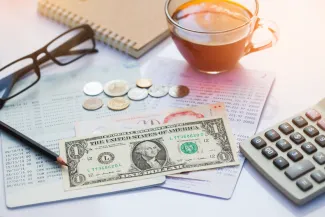 Financial statement with assorted United States currency and coins, calculator, eyeglasses, and a cup of coffee on top.