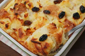 Tray of cooked old fashioned bread pudding with a serving utensil.