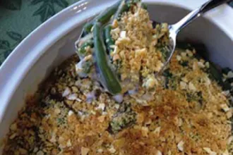 Close up view of a serving dish of green bean casserole with a serving utensil of casserole held just above.