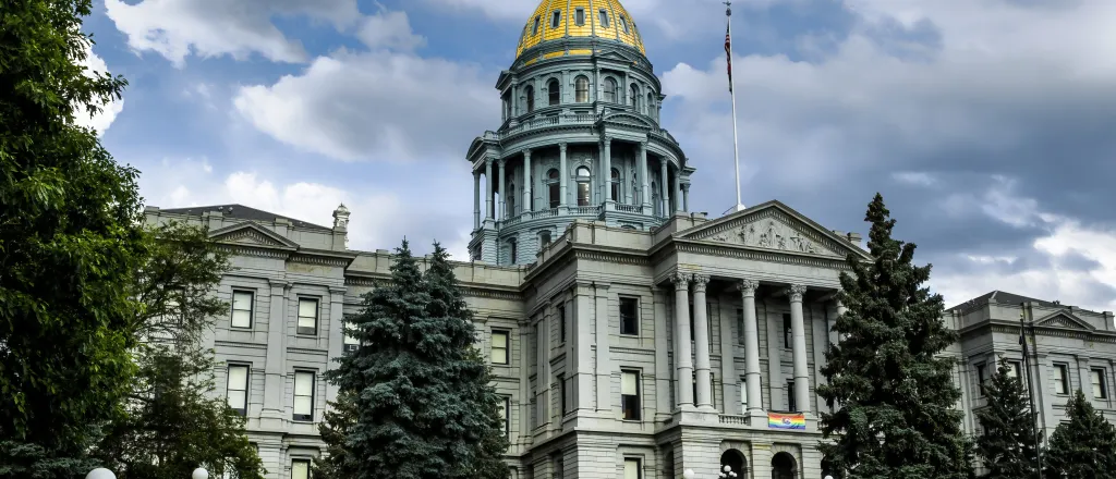Colorado State Capitol Building fronted by green trees under a cloudy sky