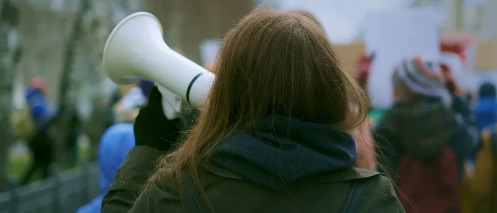 View from behind of a person holding a megaphone at a protest rally.
