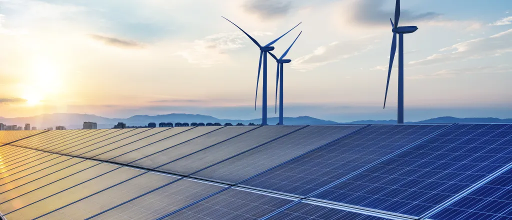 Solar panels with wind turbines in the background.