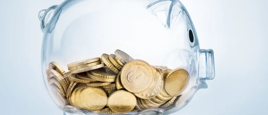 Glass piggy bank half filled with gold coins