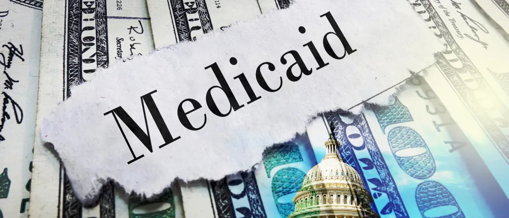 A scrap of torn paper with the word "Medicaid" rests on top of a spread of United States 100 dollar currency.