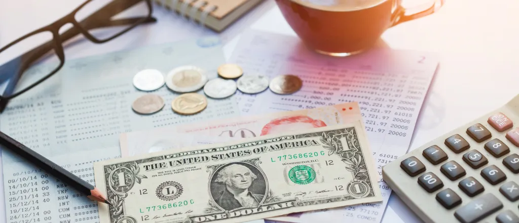 Financial statement with assorted United States currency and coins, calculator, eyeglasses, and a cup of coffee on top.