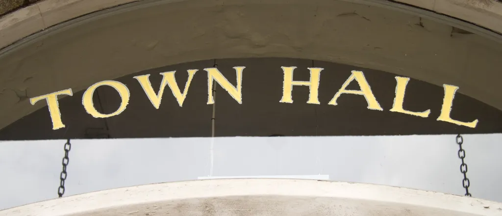 Close up of a door to a building with a glass transom above. The words "Town Hall" are stenciled on the glass in gold leaf foil.