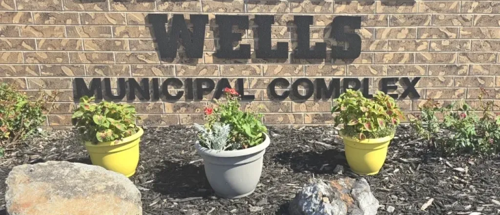 Brick wall with the words Cheyenne Wells Municipal Complex. Assorted potted plants and rocks are on mulched ground in front of the sign.