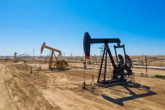 Oil pumping rigs closely spaced on bare ground under a blue cloudless sky