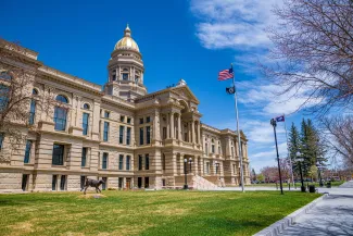View of the Wyoming State Capitol Building from an angle. A flagpole with the United States and Wyoming flags is in front.