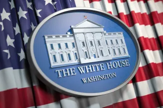 Close up of an oval, carved plaque with an image of the White House. The plaque is on top of a flag of the United States of America.