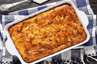 Casserole dish of Matzo Meal Kugel on a cloth next to a serving utensil.